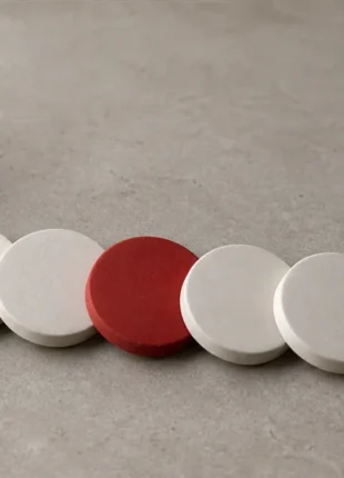 A plain two-part plaster mould lying open on a warm grey surface beside a row of five identical pale cast discs, the middle one scarlet, an illustration of the AI website builder vs web agency question: the copies are cheap, the mould is not